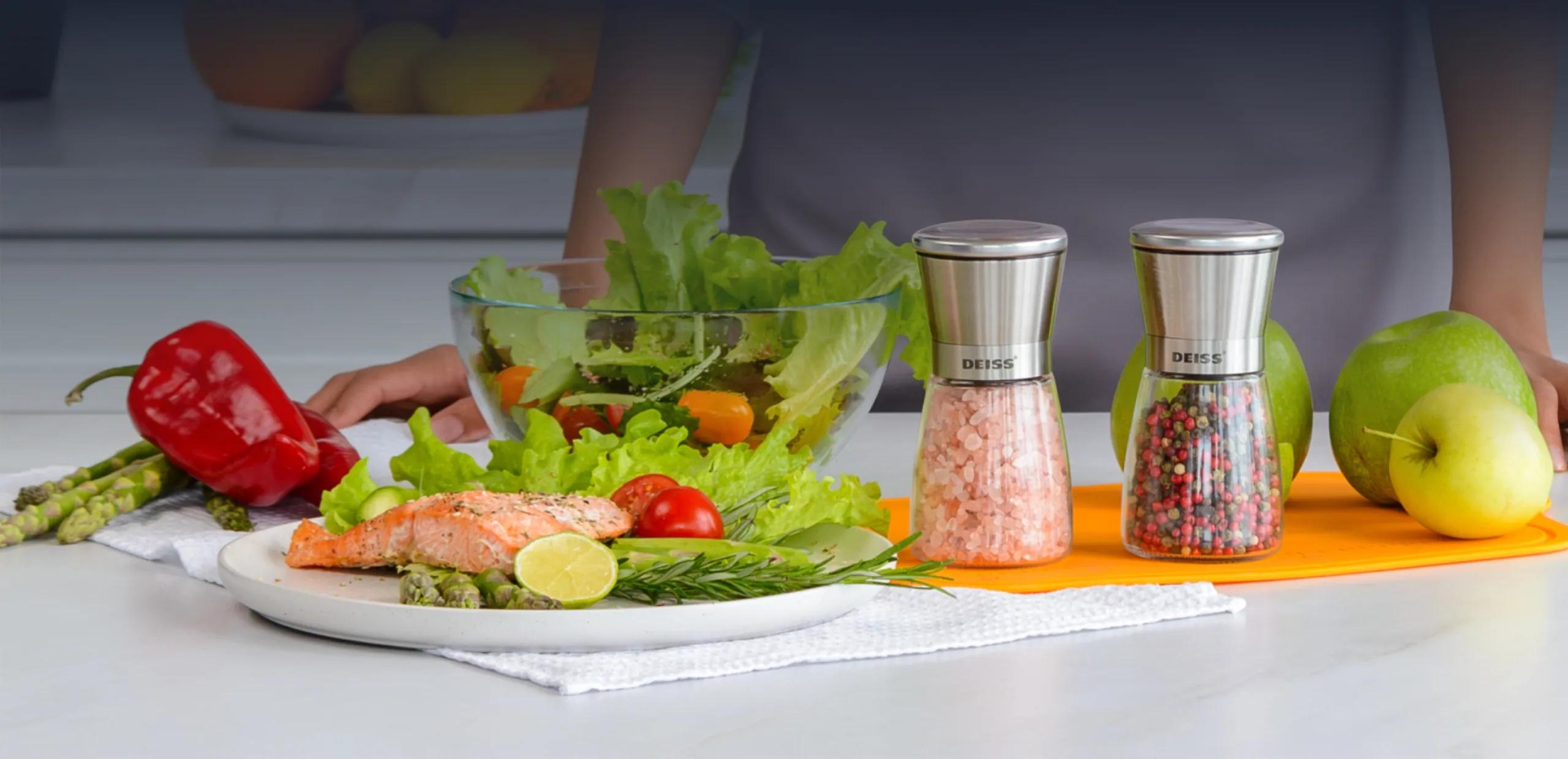 Deiss PRO salt and pepper mills with pink salt and peppercorns beside a salmon salad